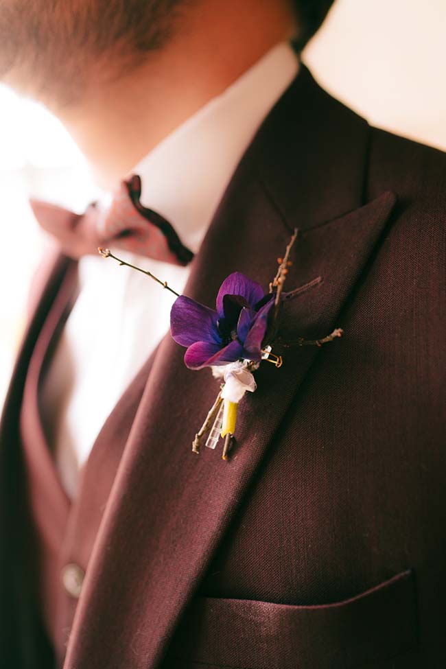 Un boutonnière élégant sur un costume noir, avec une fleur violette et blanche, met en valeur l'élégance et la