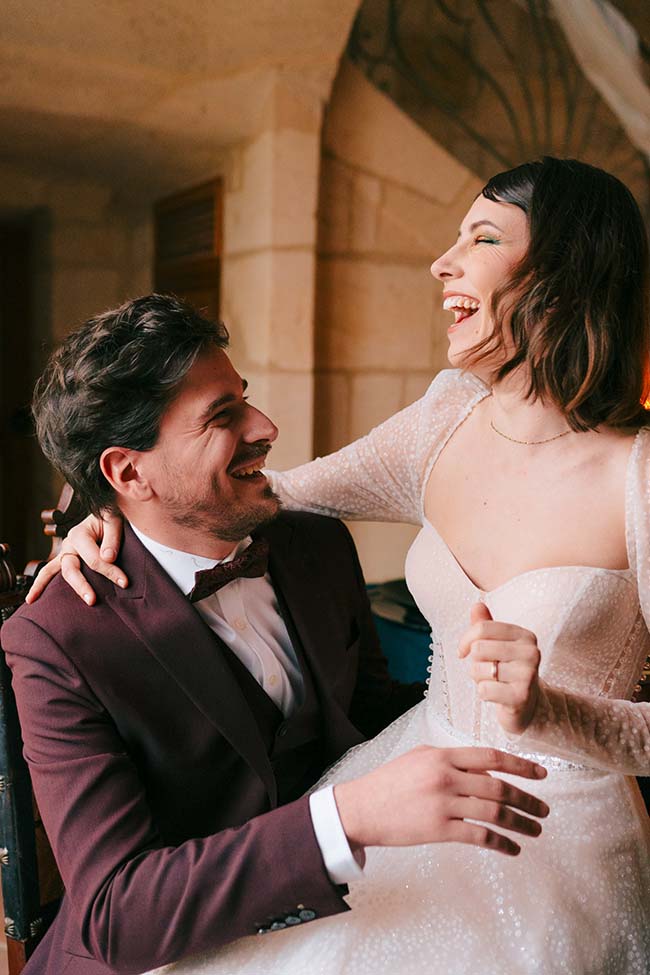 Un couple heureux dans des vêtements de mariage classiques partageant un moment de joie intime dans un décor romantique.
