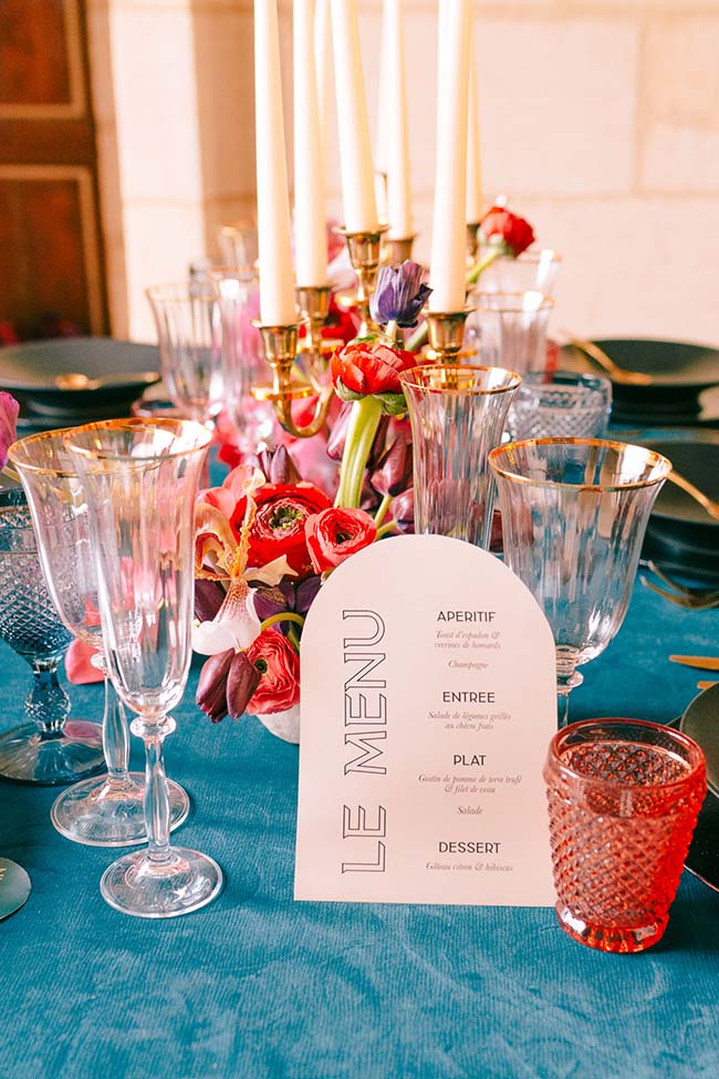 Tableau de banquet moderne et coloré, avec un menu soigné et des bougies, pour un mariage vivant et contemporain.