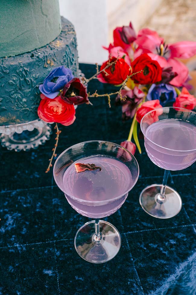 Un mariage moderne et vibrant avec un gâteau en forme de tour et des verres de cocktails violets, entourés de fleurs vives.