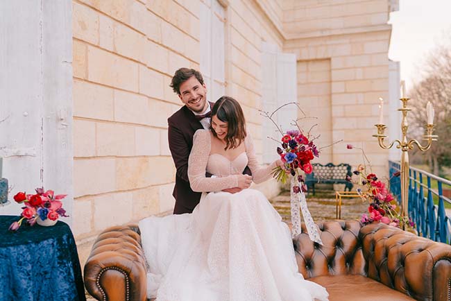 Un couple heureux dans des costumes de mariage classiques, entourés de fleurs vives et de meubles luxueux, incarnant un