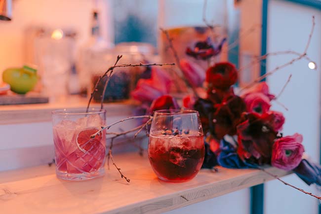 Un mariage moderne et vibrante, avec un plateau de fruits colorés et des verres de vin rouge, entourés de fleurs
