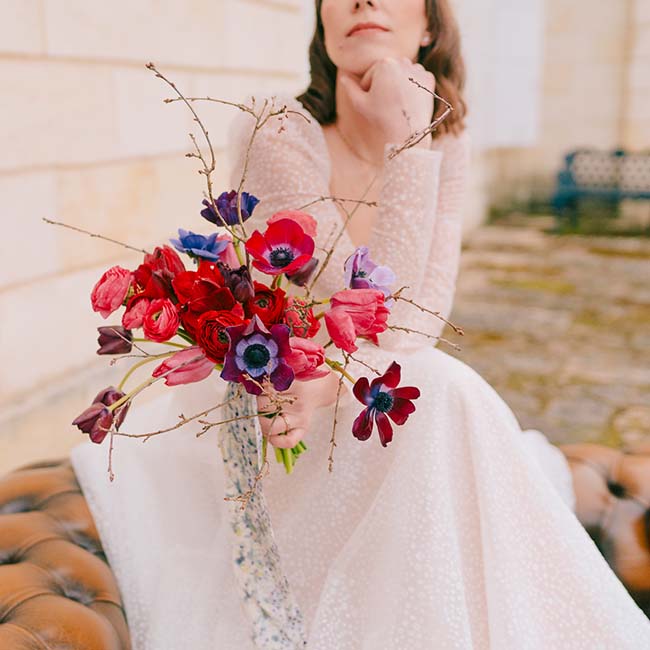 Une mariée en robe blanche tendue tient un bouquet de fleurs vives, créant un contraste saisissant avec son habillement.