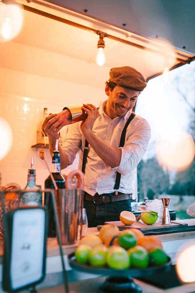Barman riant et habillé de mode, préparant un cocktail au bar d'un camion, avec un fond doux et accents lumineux,