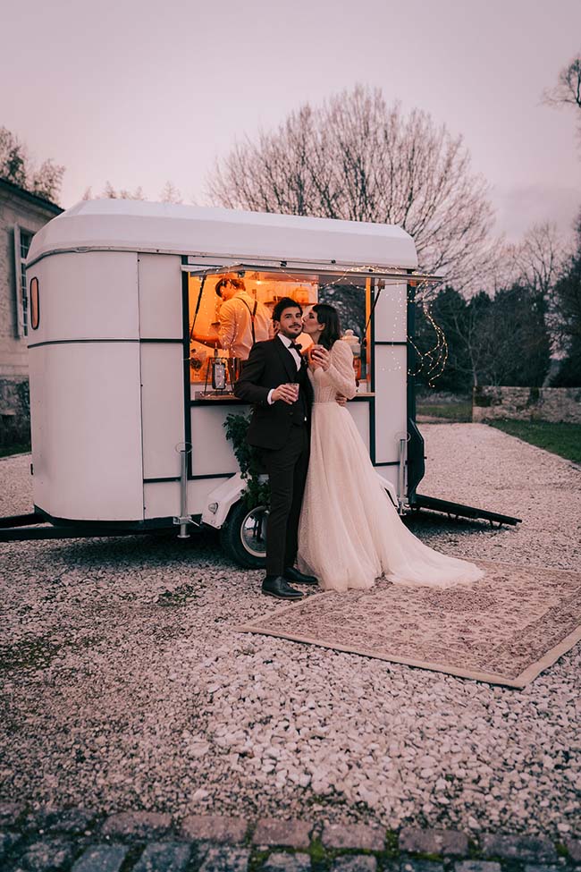 Un couple marié et délicieux se détient devant un camion food, décoré de guirlandes lumineuses, créant un atmosphère