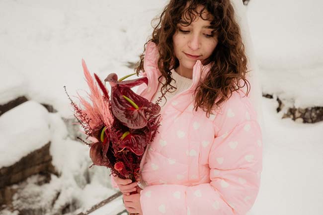 Une jeune femme dans une doudoune rose émerveillée par sa fleur de neige.