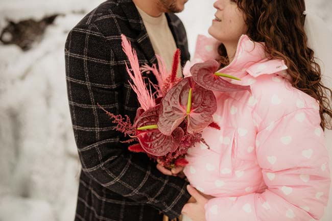 Un couple romantique partageant un moment tendre au cœur d'hiver, entouré de fleurs sauvages rouges, dans un contexte