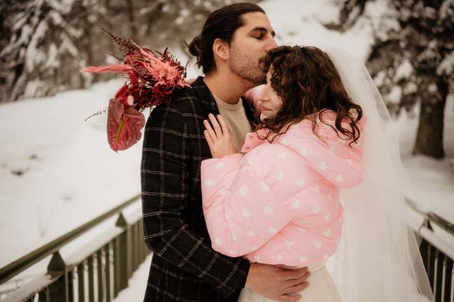 Un couple romantique partage un moment intime dans un décor hivernal charmant, vêtu d'un manteau rose doux et d'un costume sombre.