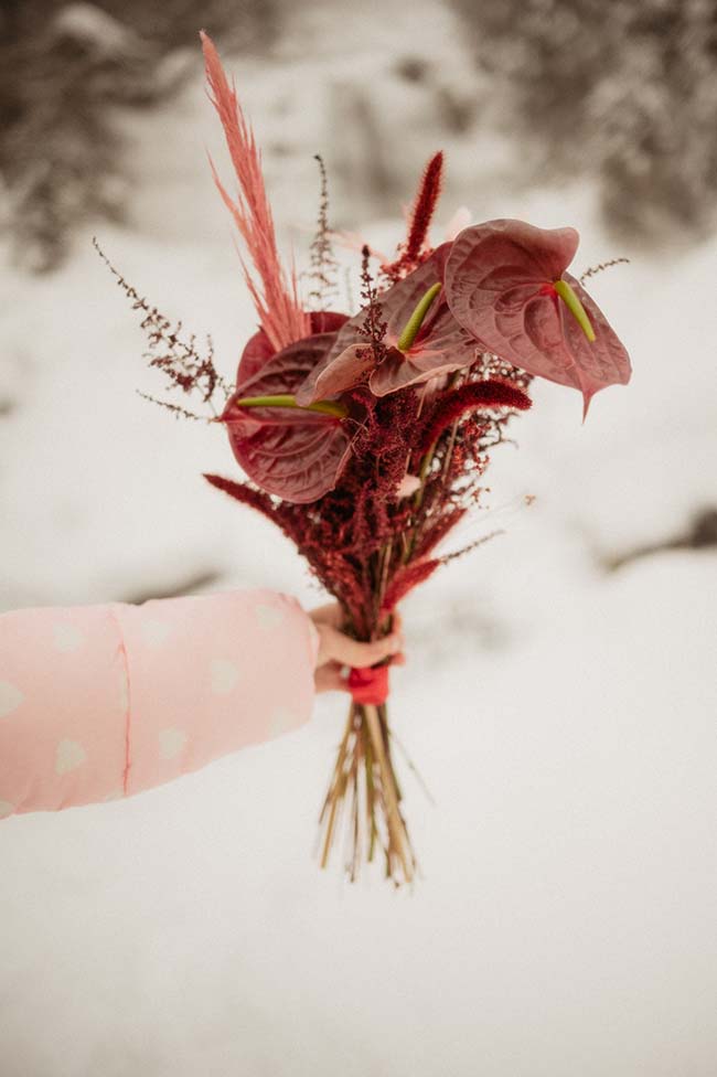 Un bouquet romantique de fleurs rouges et vives dans une main rose, contre un fond de neige douce.