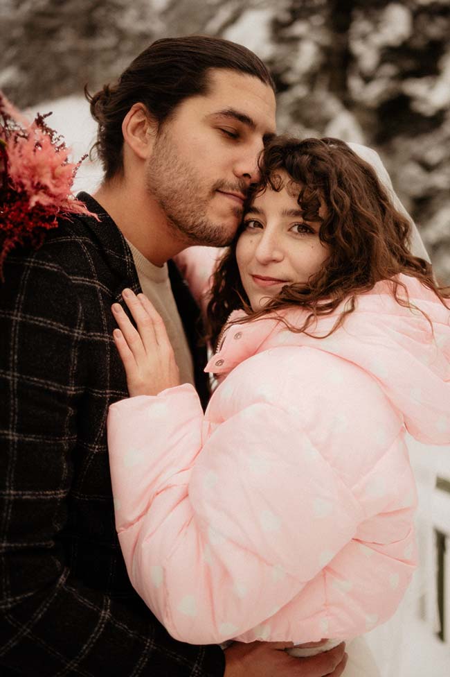 Un couple heureux dans une ambiance romantique sous la neige, l'homme en costume et la femme en doudoune rose.