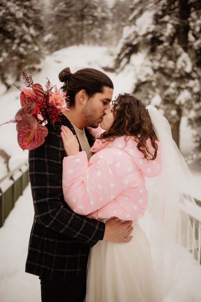 Un couple de mariage émotionnellement partageant un baiser intime dans un décor neigeux, avec la mariée vêtue d'un