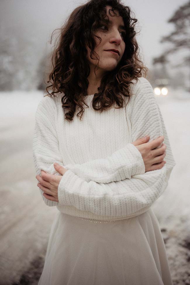 Une jeune femme dans un vêtement blanc chaud dans un paysage enneigé, incarnant l'ambiance romantique d'un mariage sous la neige.