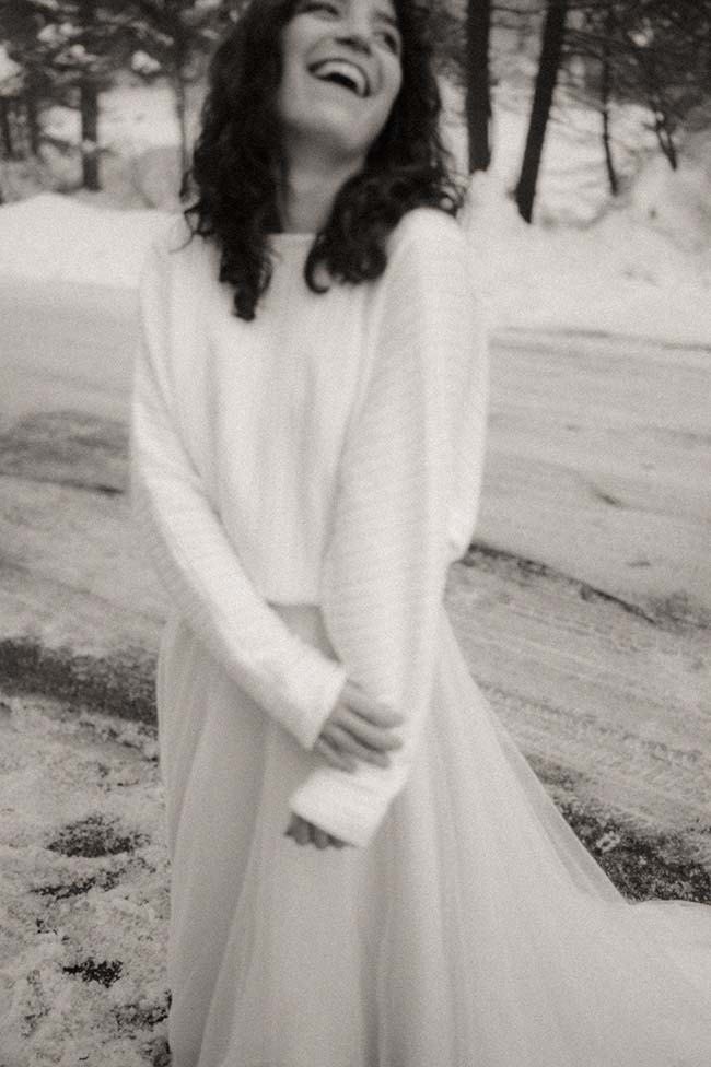 Une jeune femme souriant dans une robe blanche, dans un décor de neige, incarnant la beauté et la joie du mariage sous la neige.