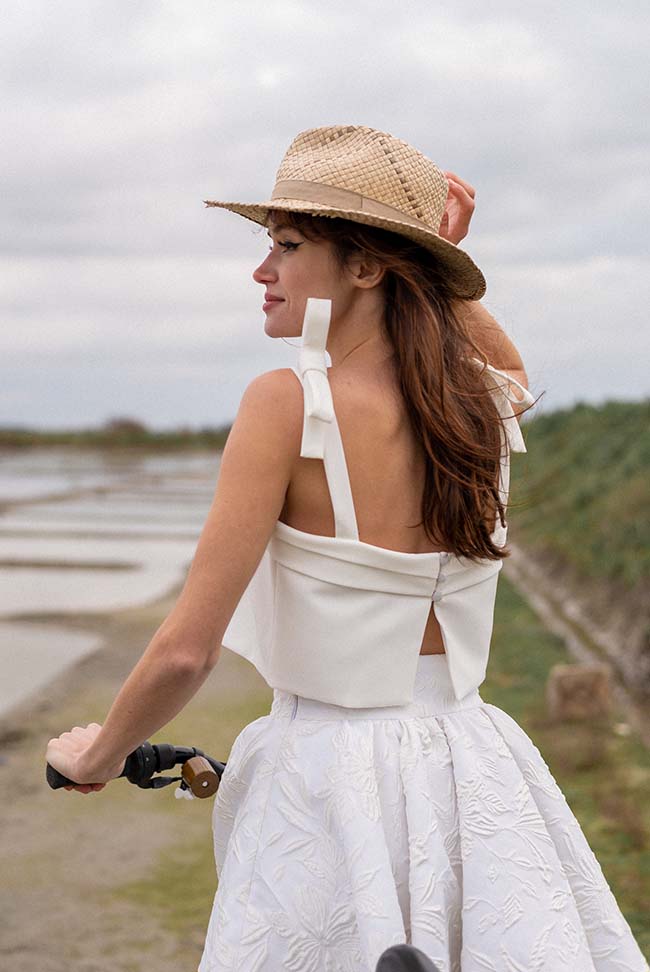 Une jeune femme en robe blanche élégante et chapeau de paille, évoluant dans un décor paisible de rivage, incarnant