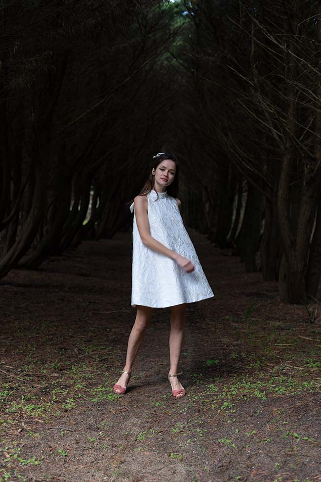 Une jeune femme dans une robe blanche élégante se tient dans un bois serein, créant un atmosphère romantique et paisible.