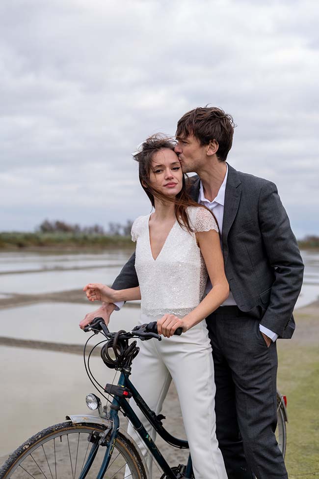 Un couple romantique à vélo, célébrant leur amour à travers des vêtements élégants contre un décor paisible.
