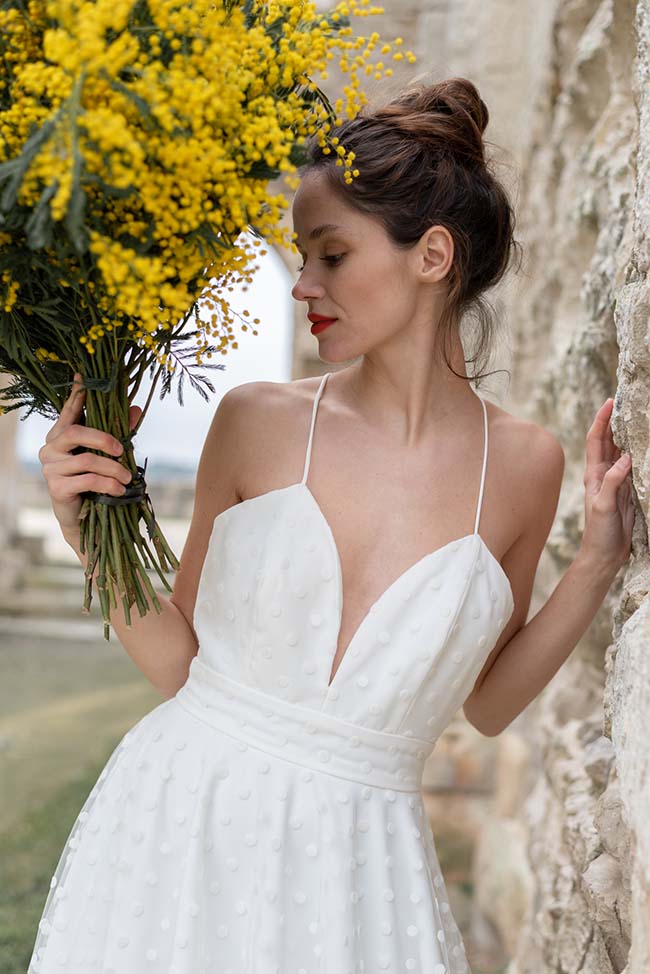 Magnifique mariée en blanc tendre tenant un bouquet de fleurs jaunes, évoquant l'optimisme et la joie.