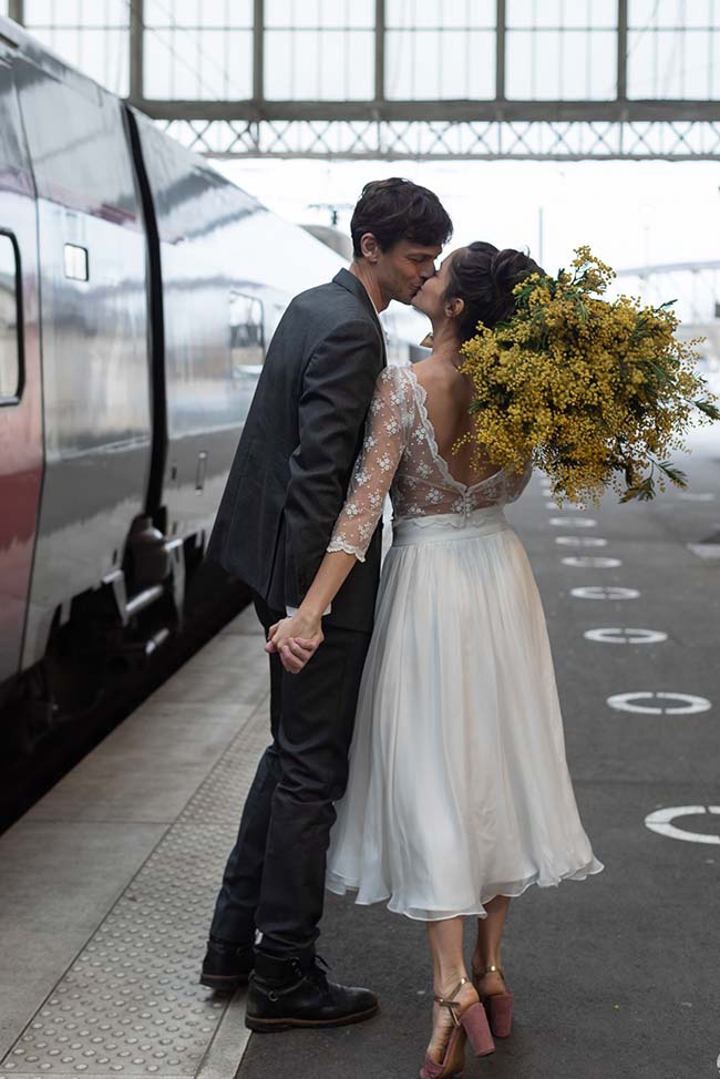 Un couple romantique en robe de mariage et costume, partageant un baiser tendre à côté d'un train, incarnant l'élégance