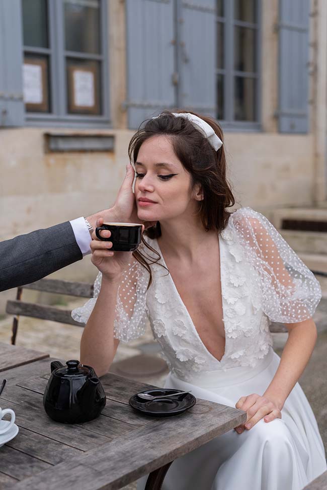 Une jeune femme dans un vêtement de mariage romantique savoure un café chaud avec un compagnon, dans un décor charmant et intime.