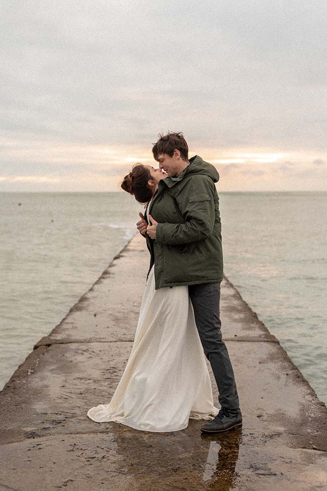 Un couple romantique partage un moment tendre sur un quai pluvieux, évoquant la beauté sentimentale de la vie.
