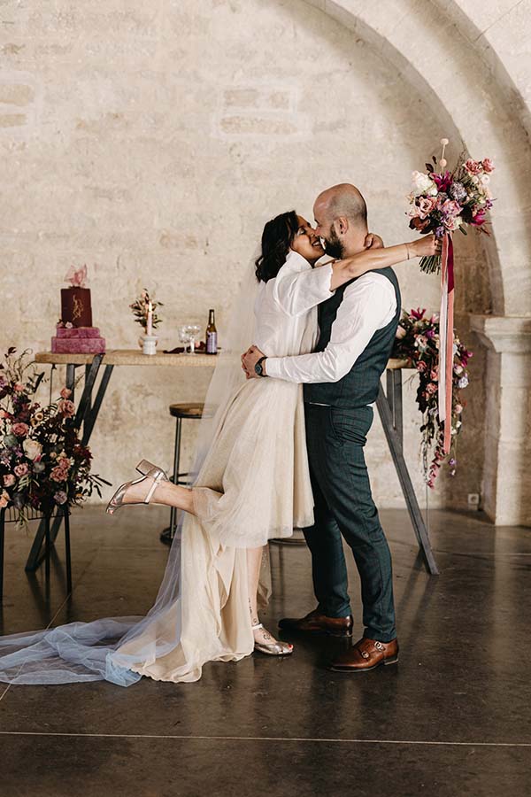 Un couple en amour partageant un baiser tendre dans un décor romantique avec des fleurs et un gâteau de mariage.
