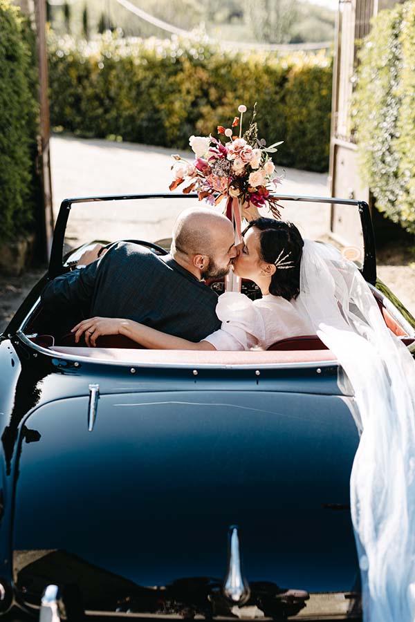 Un couple romantique dans une voiture vintage, célébrant leur mariage avec des fleurs colorées et une ambiance joyeuse.