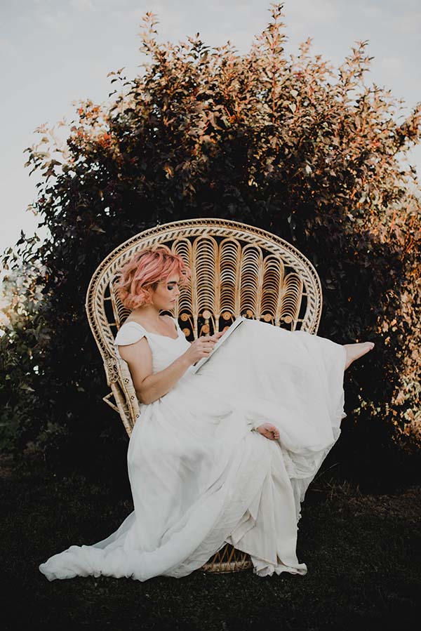 Élégante mariée en blanc, assise sur un fauteuil en rattan orné d'un motif floral, plonge dans l'ambiance paisible de la nature.