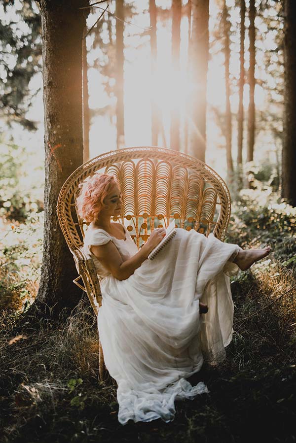 Une mariée en robe blanche légère s'adonne à la lecture dans un fauteuil en rattan, baignée dans une lumière douce du soleil.