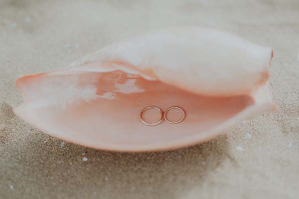 Rings de mariage dans un coquillage rose sur la plage, un instant romantique pour un mariage en Pays de Loire.