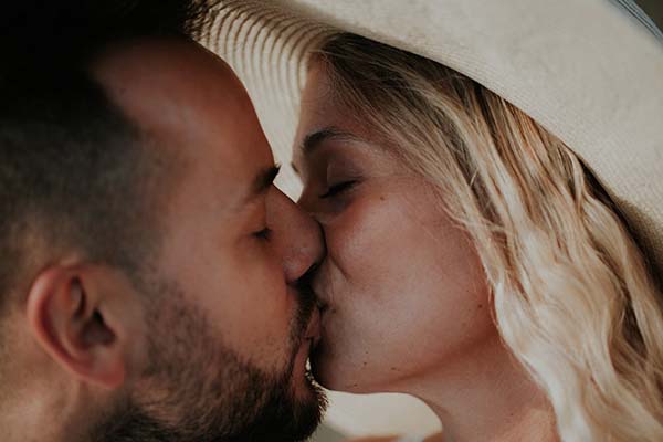 Un couple romantique partage un baiser tendre sous un chapeau de paille, parfaite pour un mariage en bord de mer dans