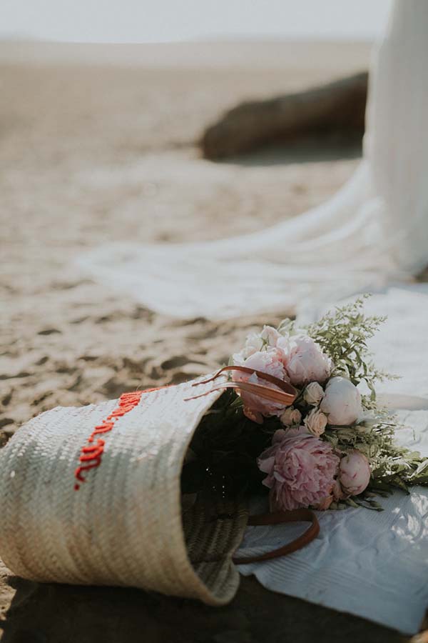 Un bouquet de fleurs doux reposant sur une serviette blanche, avec un sac à main en osier à proximité, évoquant un