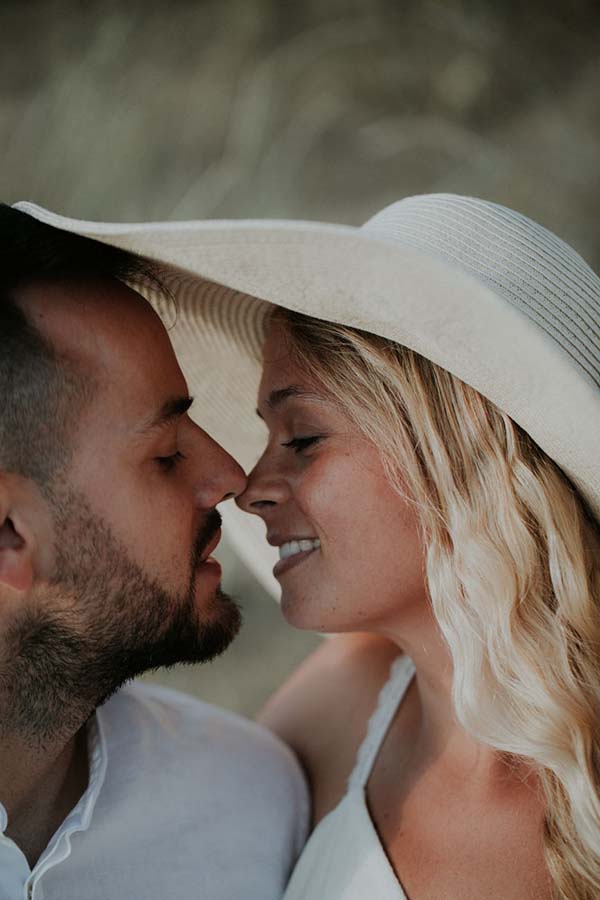 Un couple heureux se penche l'un envers l'autre sur une plage paisible, évoquant l'ambiance romantique d'un mariage en