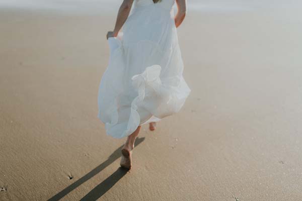 Magnifique scène de plage avec une mariée en robe blanche légère, idéale pour un mariage en bord de mer dans le Pays de Loire.