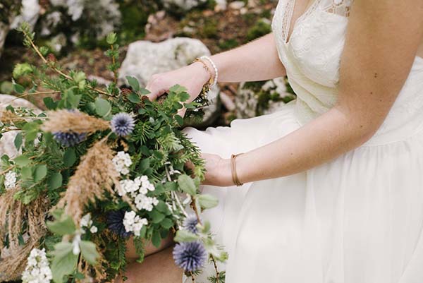 Une bride en robe blanche tend les fleurs de son bouquet dans une scène paisible au cœur des Alpes.