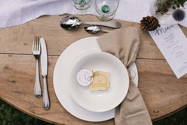 Tableau élégant avec assiettes blanches et serviette beige, décorant un mariage en plein air dans les Alpes du Rhône.