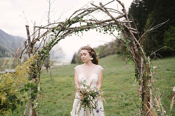 Élégante mariée dans un champ verdoyant, son arch de végétation suggérant un mariage intime et romantique dans les Alpes du Rhône.