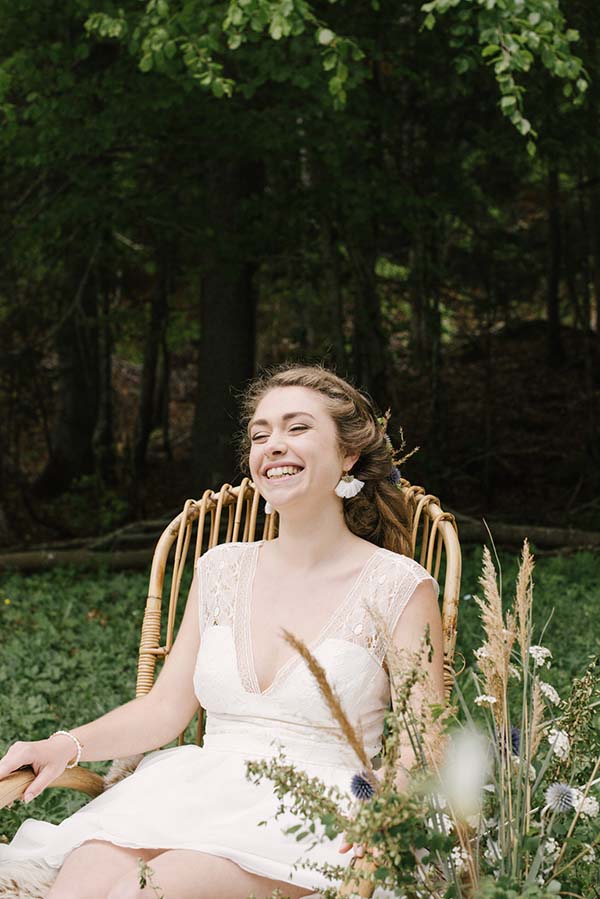 Une jeune mariée dans un joli robe blanche se détend dans un fauteuil en ratt, entourée de fleurs et de végétation