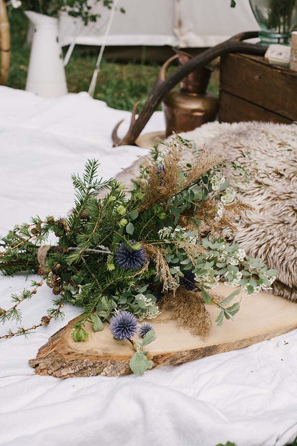 Un bouquet romantique de fleurs et de feuilles reposant sur un tronc de bois, encadré par des accessoires naturels,
