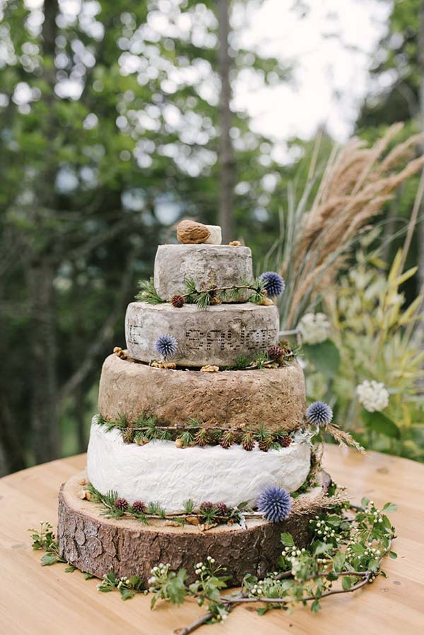 Un gâteau de mariage en forme de tourbière, décoré de conifères et de fleurs, sur un plateau en bois, dans un décor verdoyant.