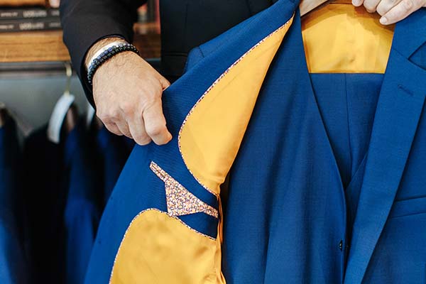 Un tailleur présente un costume bleu et jaune avec un motif audacieux, dans un magasin de vêtements.