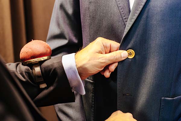 Un homme en costume met un bouton unique sur son vestiaire, prêt à se présenter à son mariage.
