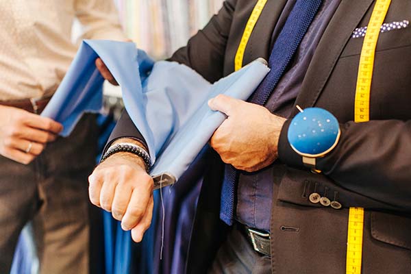 Tailleur en costume en train de mesurer un pantalon bleu, ambiance professionnelle et soignée.