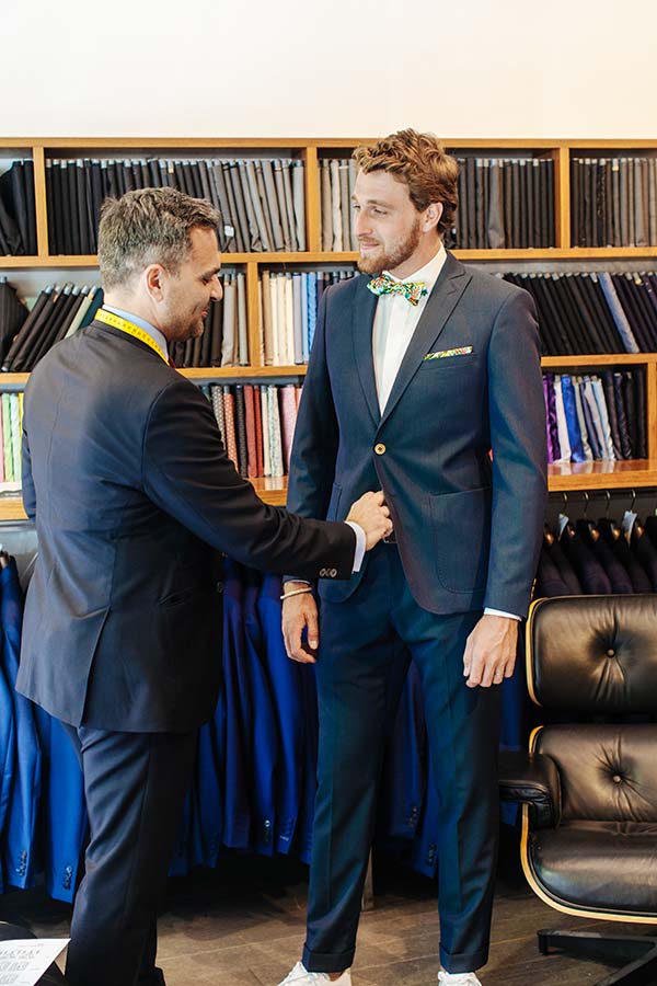 Un homme de soins détaillé ajuste un costume de mariage pour un jeune homme dans un magasin de vêtements de mariage élégant.