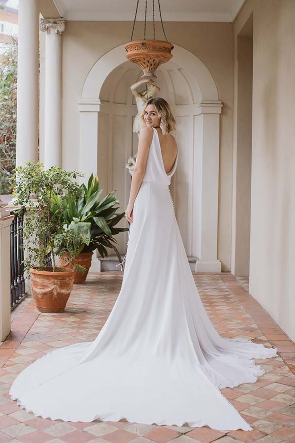 Élégante mariée en robe blanche avec dos ouvert, se tenant sur une cour intérieure charmante avec des pots de plantes.