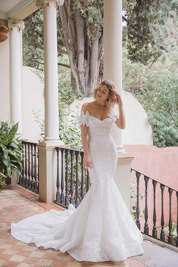 Une mariée dans un magnifique robe de mariage blanc avec des détails délicats et un train long, debout sur une terrasse