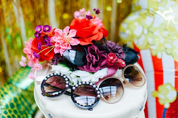 Un photobooth vibrante avec des lunettes de soleil et des fleurs colorées, idéal pour un mariage ensoleillé.