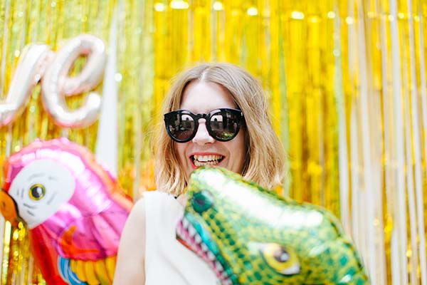 Une jeune femme souriant avec des ballons animaux colorés contre un fond de soie dorée, idéale pour un photobooth de