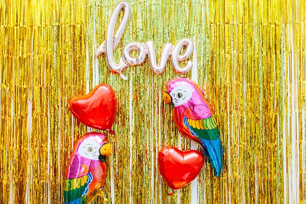 Photobooth vibrante avec ballons en forme de coeur et de perroquet colorés contre un fond de soie dorée, idéale pour un