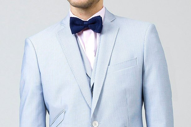 Un costume bleu pâle avec un nœud bleu et un boutonnière, parfait pour un mariage élégant.