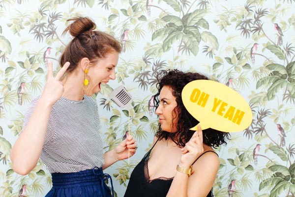 Amis joyeuses dans un photobooth coloré, incarnant l'essence de la fête et des accessoires de mariage.